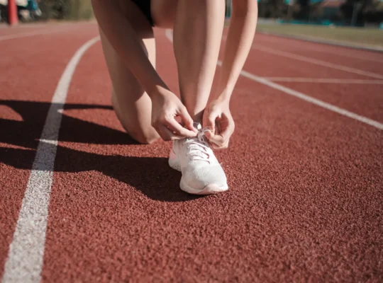Läuferin bindet ihre weißen Sportschuhe auf einer Laufbahn; redaktionelles Symbolbild für den Sportartikelmarkt und die Adidas-Analyse.