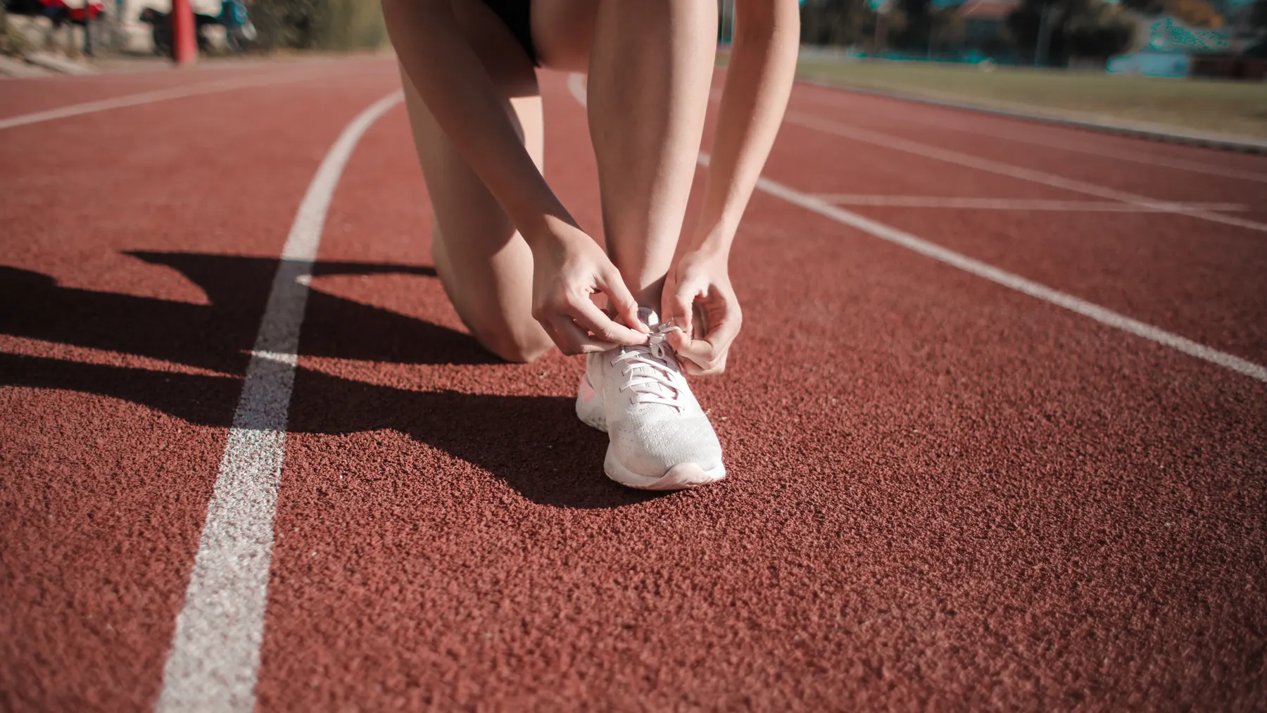 Läuferin bindet ihre weißen Sportschuhe auf einer Laufbahn; redaktionelles Symbolbild für den Sportartikelmarkt und die Adidas-Analyse.