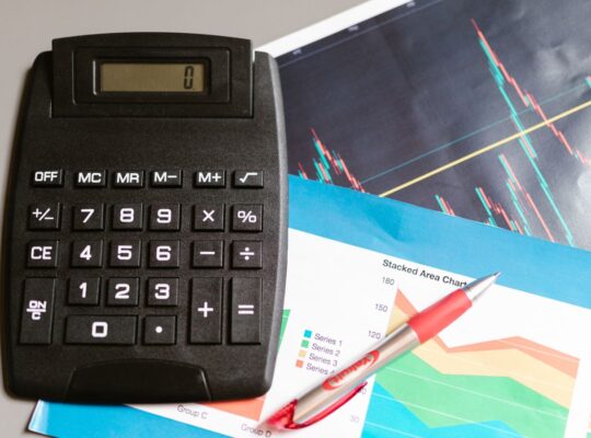 Finanzarbeitsplatz mit Rechner, Stift und Finanzcharts als Symbol für Enterprise Value, Schulden, Cash und Unternehmensbewertung.