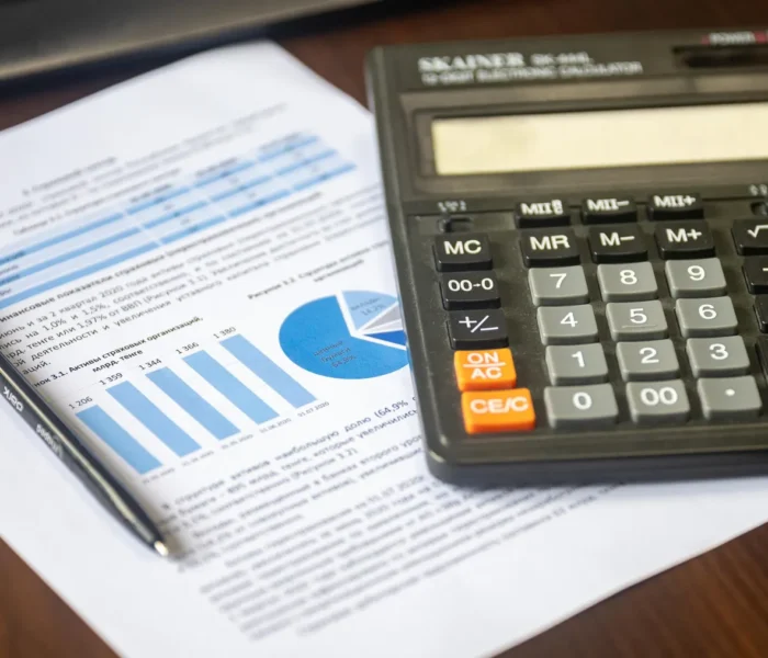 Kalkulator, Finanzbericht und Stift auf einem Schreibtisch als Symbol für die Berechnung der Free-Cashflow-Rendite von Aktien.