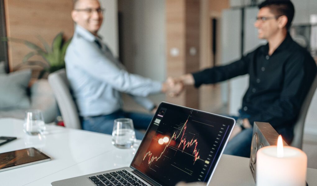 Geschäftspartner bei einer Unternehmensvereinbarung mit Finanzchart als Symbol für Übernahmen, Goodwill und mögliche Wertminderungen.
