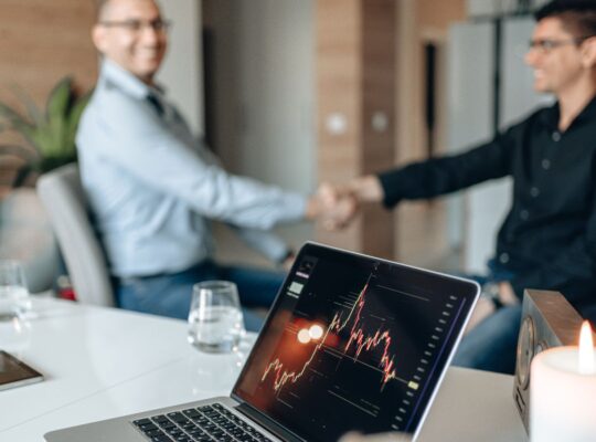 Geschäftspartner bei einer Unternehmensvereinbarung mit Finanzchart als Symbol für Übernahmen, Goodwill und mögliche Wertminderungen.