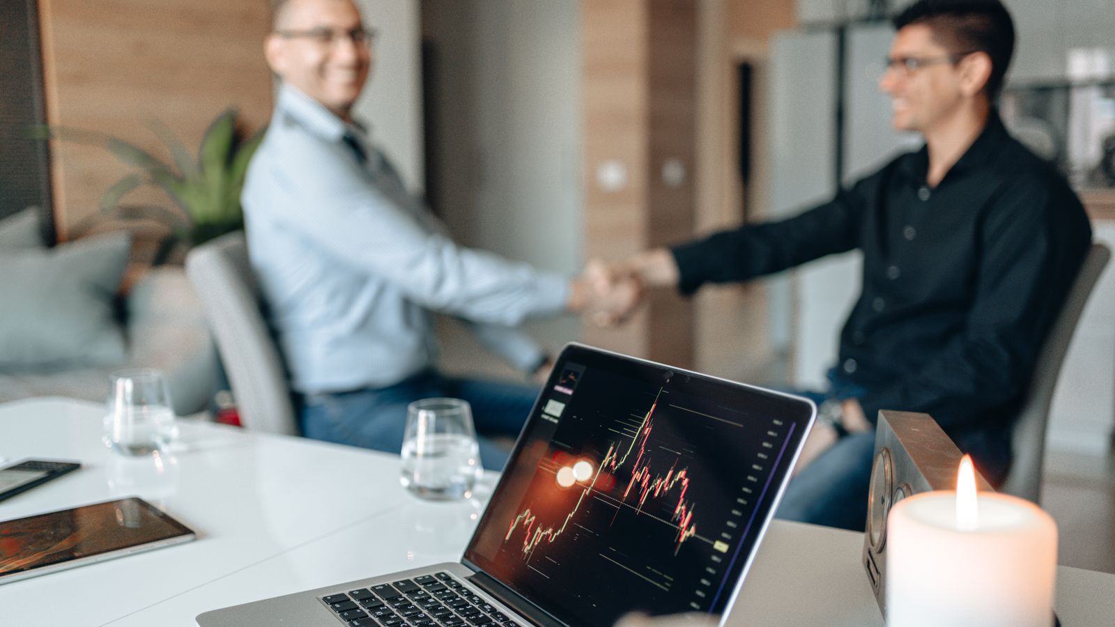 Geschäftspartner bei einer Unternehmensvereinbarung mit Finanzchart als Symbol für Übernahmen, Goodwill und mögliche Wertminderungen.
