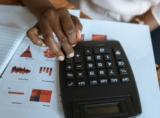 Finanzanalyst berechnet mit einem Taschenrechner Bilanzkennzahlen anhand von Diagrammen und Unterlagen, ohne hinzugefügte Schrift.