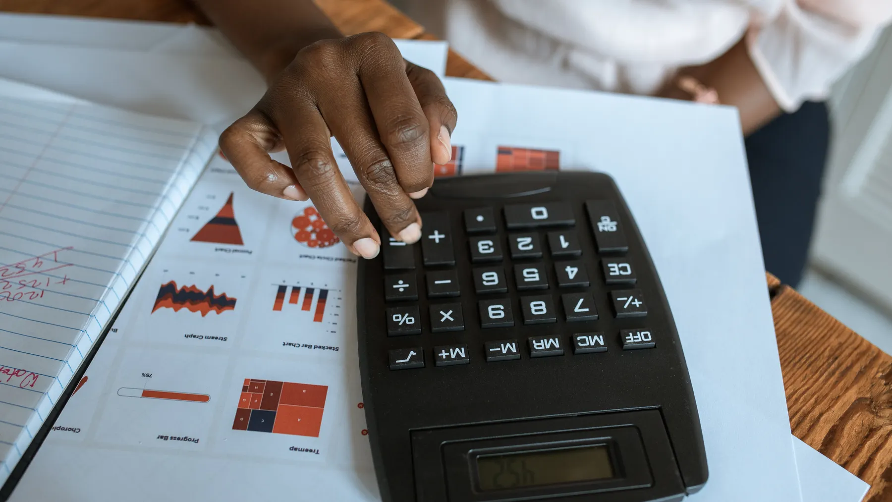 Finanzanalyst berechnet mit einem Taschenrechner Bilanzkennzahlen anhand von Diagrammen und Unterlagen, ohne hinzugefügte Schrift.