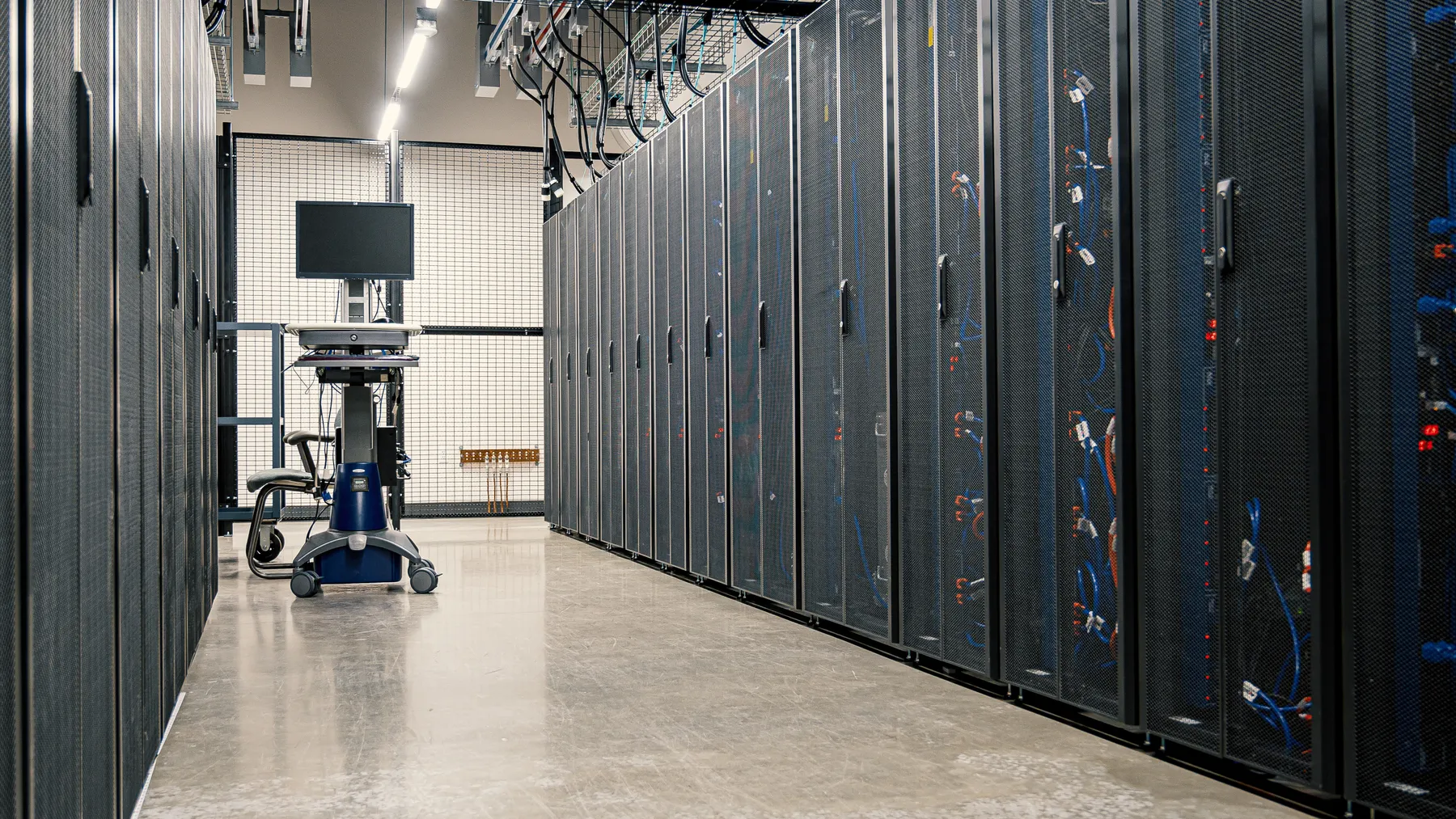 Technischer Gang zwischen Server-Racks und Kabelanlagen eines modernen Rechenzentrums als Motiv für Stromversorgung und Kühltechnik.