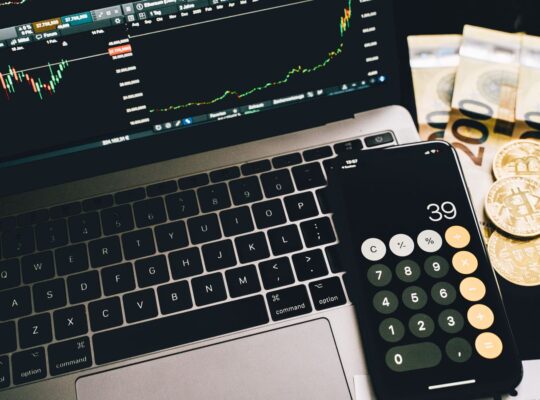 Finanzarbeitsplatz mit Rechner, Marktcharts und Geld als Symbol für Nettoverschuldung, EBITDA und Schuldentragfähigkeit.