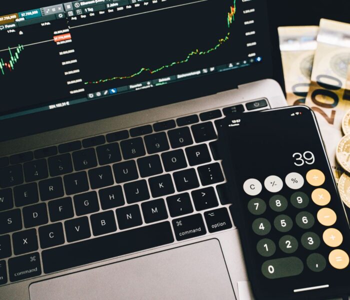 Finanzarbeitsplatz mit Rechner, Marktcharts und Geld als Symbol für Nettoverschuldung, EBITDA und Schuldentragfähigkeit.