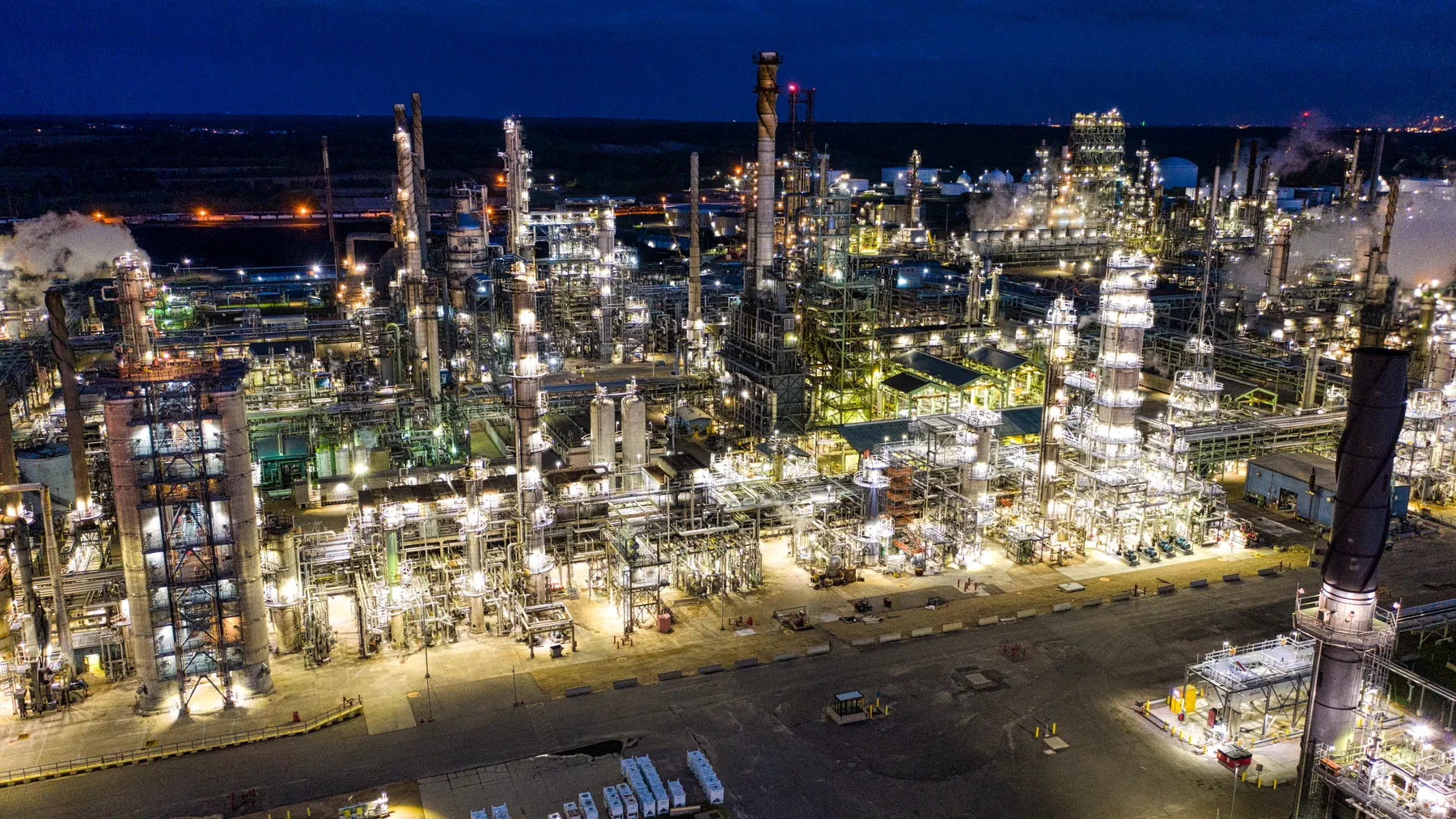 Beleuchtete Erdölraffinerie bei Nacht mit weitläufigen Industrieanlagen, Symbolbild zum Ölpreis und Kerosinkosten 2026.