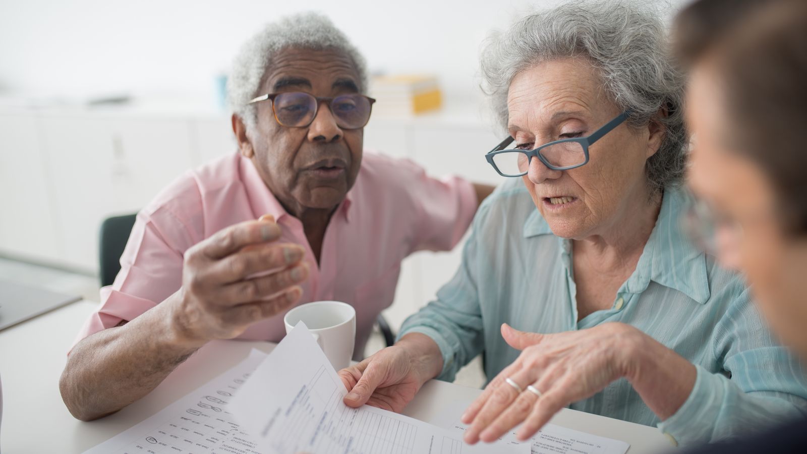 Älteres Paar bespricht Finanzunterlagen mit einem Berater als Symbol für Pensionsverpflichtungen, Altersvorsorge und langfristige Unternehmenszusagen.
