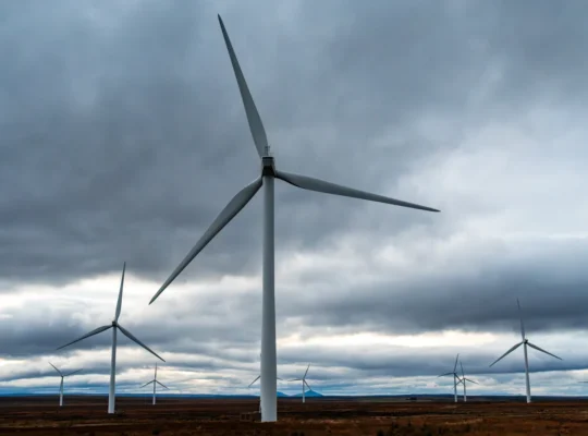 Mehrere moderne Windenergieanlagen auf weitläufigen Feldern unter dramatischen Wolken; Symbolfoto für Risiken im Windpark-Projektgeschäft.