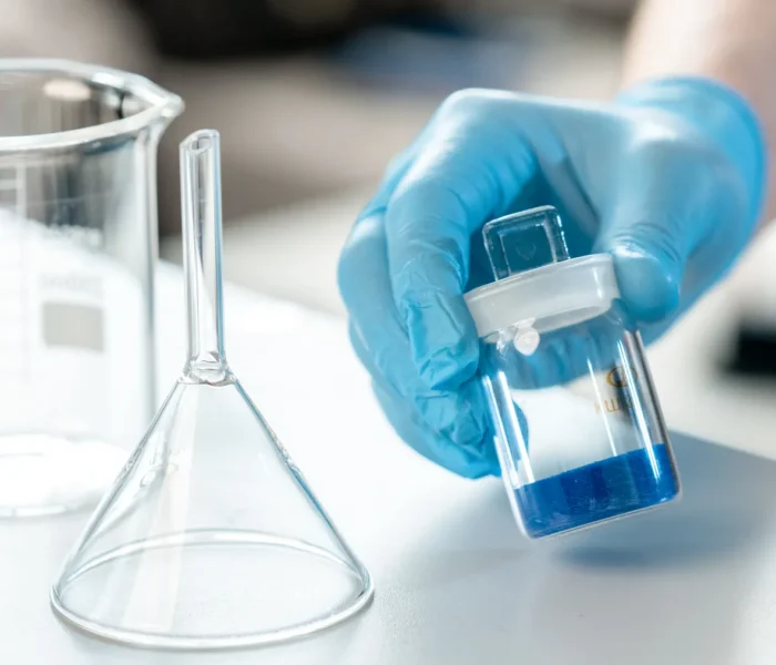Wissenschaftliche Laborarbeit mit einer Glasprobe und blauer Flüssigkeit als Symbolbild zur Roche-Analyse.