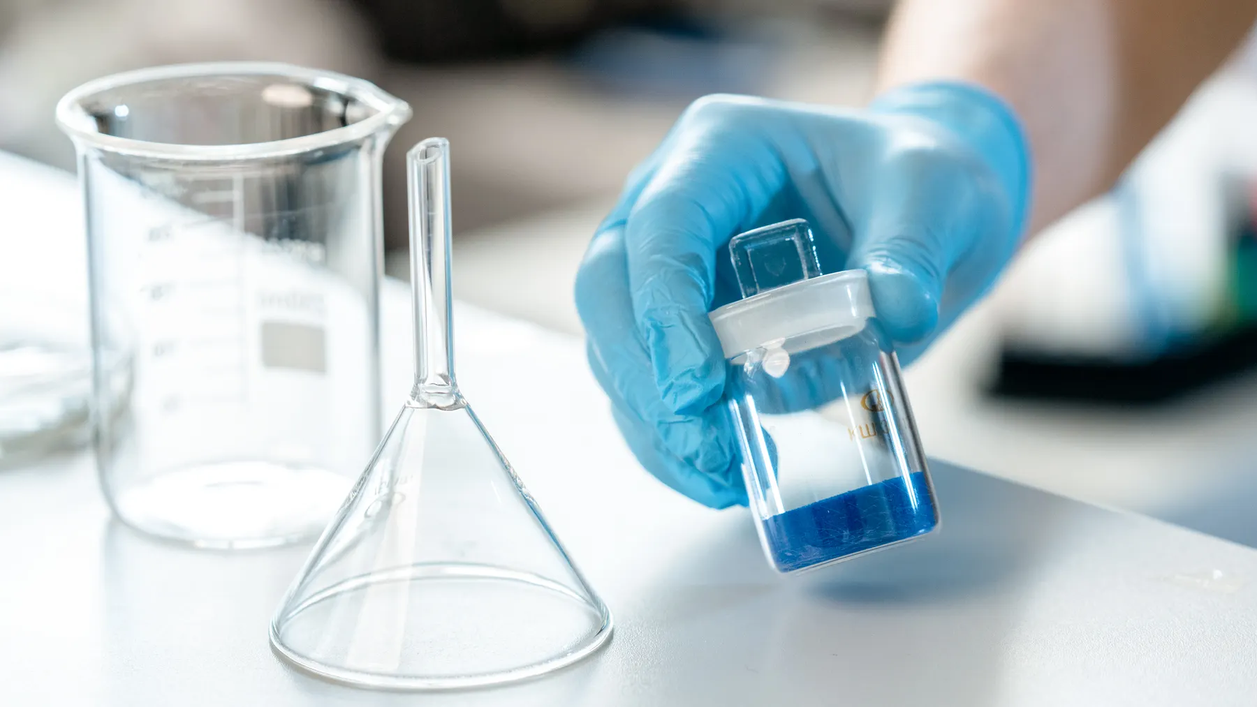 Wissenschaftliche Laborarbeit mit einer Glasprobe und blauer Flüssigkeit als Symbolbild zur Roche-Analyse.